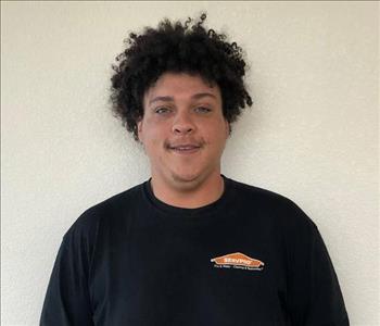 Male employee with curly hair smiling in front of a white background